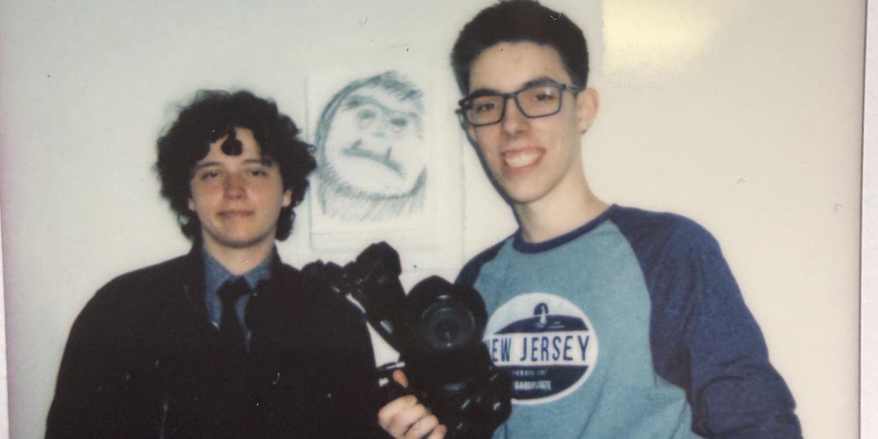 Two young men smiling, one holding a camera.