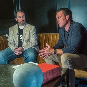 Two men engaged in a serious conversation on a couch.