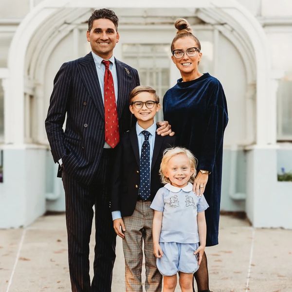 A well-dressed family of four posing outdoors in front of a white archway.