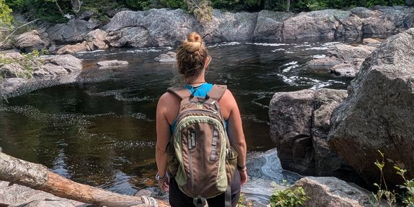 Woman with backpack overlooking a rocky river surrounded by trees.