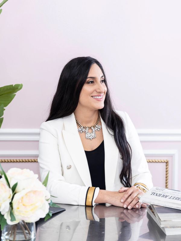 Smiling woman in white blazer sitting at a desk.
