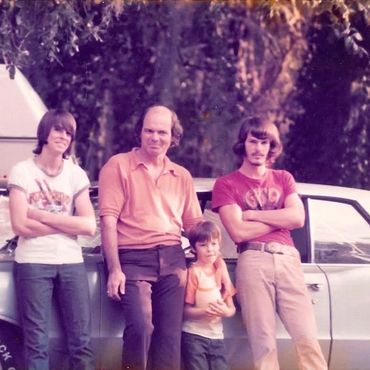 Four males posing in front of a car, likely a family photo from the 1970s.