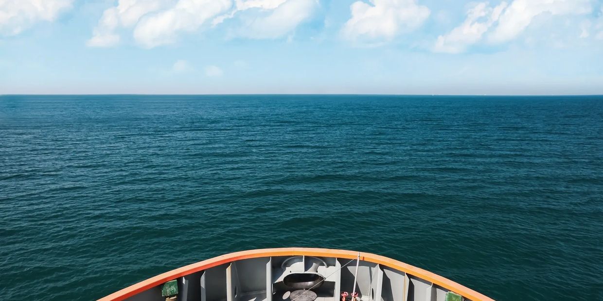 View from the bow of a ship sailing on calm ocean waters under a blue sky.
