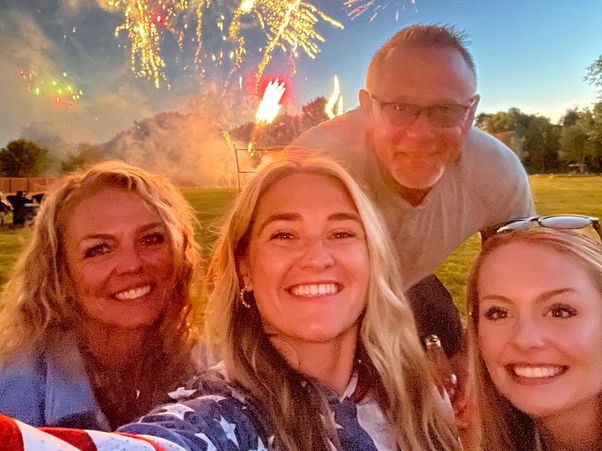 Group selfie with fireworks in the background at dusk.