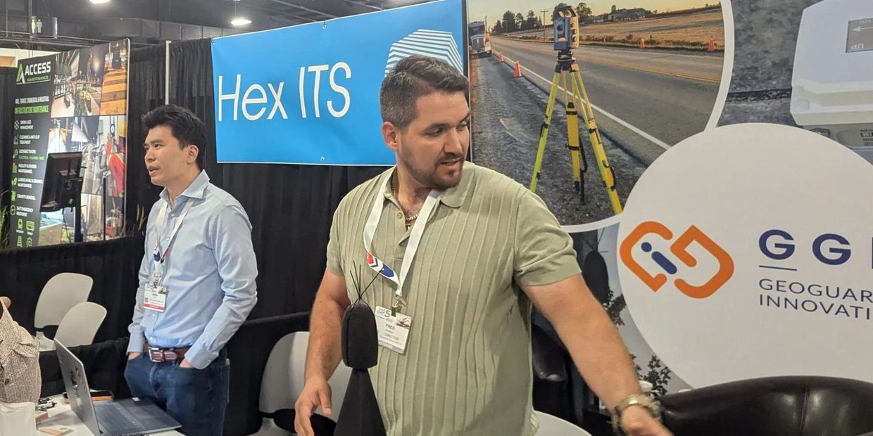Four men at a technology exhibition booth with equipment and laptops.