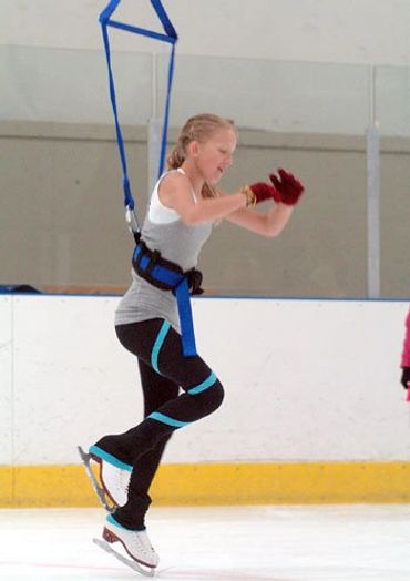 young figure skater using jump harness training system at an ice rink