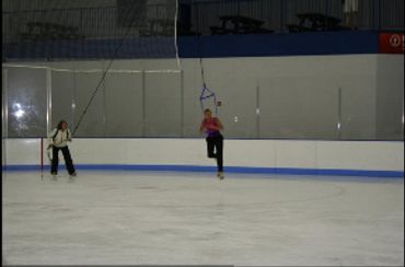 wide view of figure skaters using jump harnesses