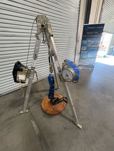 Metal tripod hoist with a harness and a winch in an industrial setting.