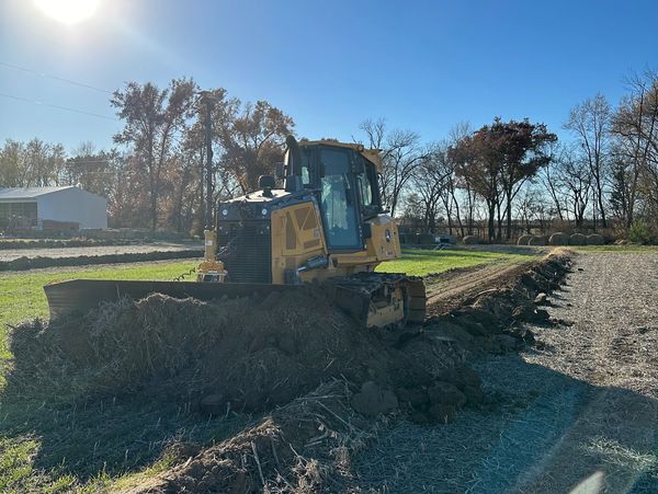 Yellow bulldozer pushing soil in a field under a bright sun.