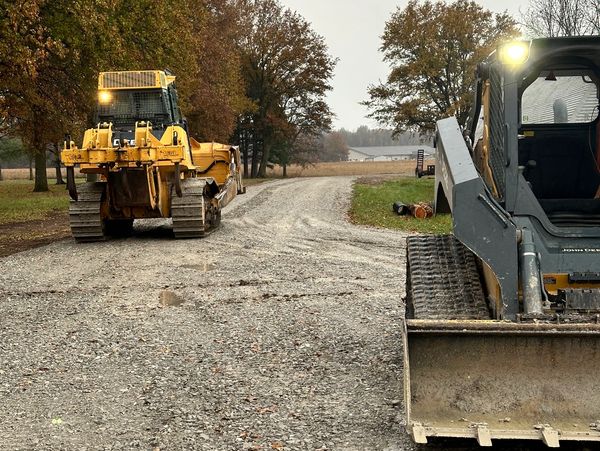 Construction vehicles on a gravel road in an autumn setting.