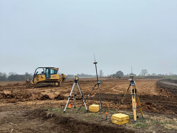 Surveying equipment set up on a construction site with bulldozers working in the background.