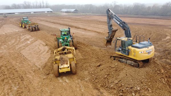 Construction vehicles working on a large dirt field, moving and digging soil.