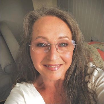 Smiling woman with glasses and long hair in a cozy room.
