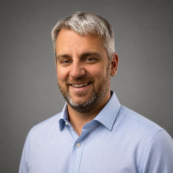 Smiling man with gray hair and beard wearing a light blue shirt.