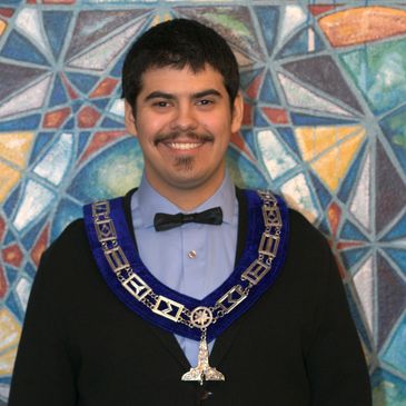 Young man smiling wearing a ceremonial chain and black bow tie.