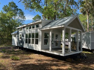 Modern tiny house with a metal roof and front porch in a wooded area.