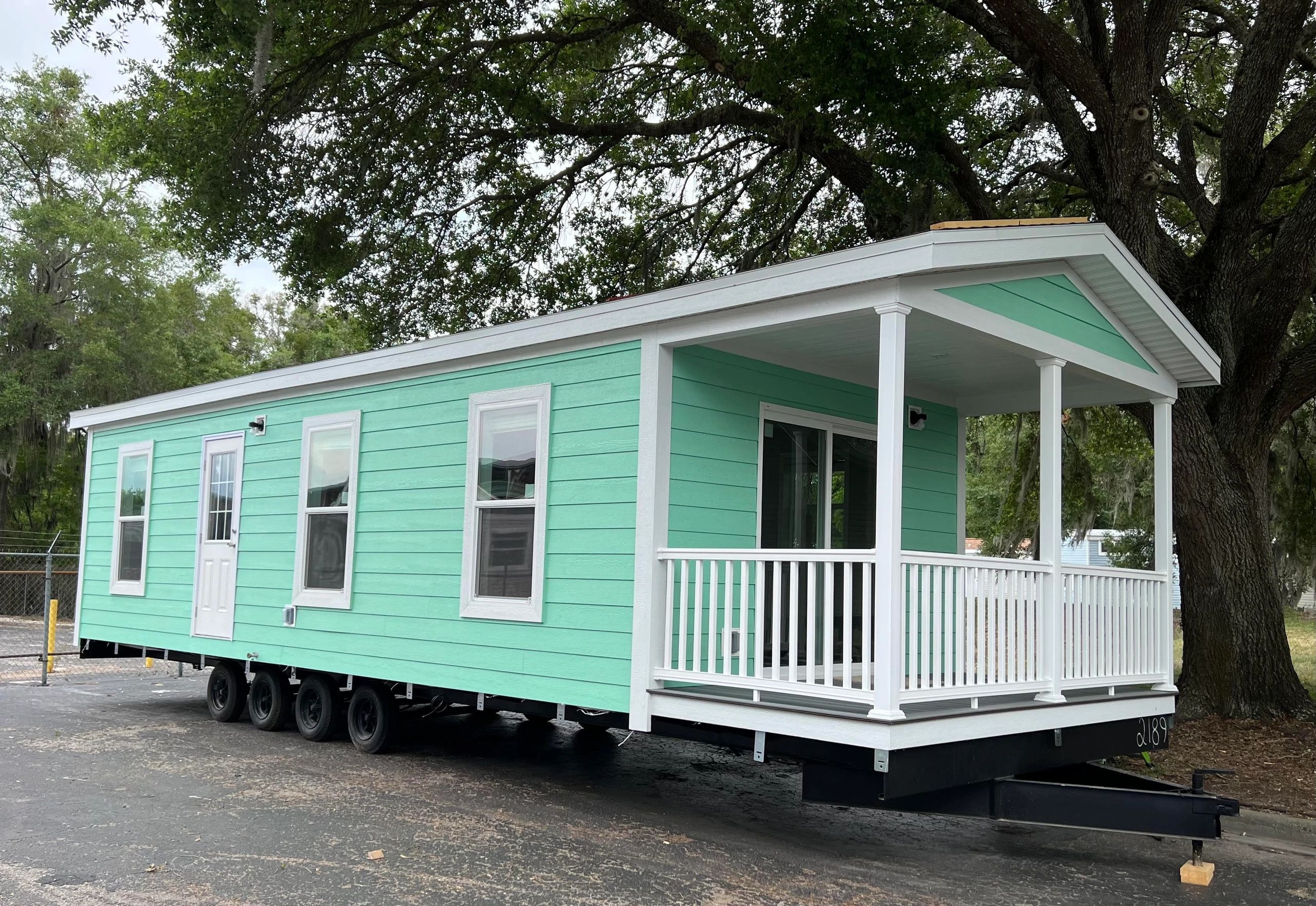 A mint green tiny house on wheels with a white porch and railing.