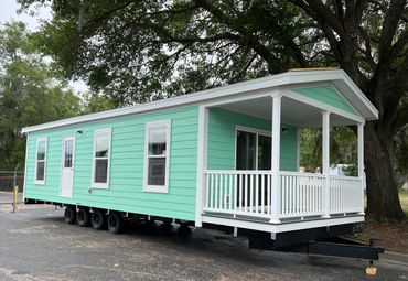A mint green mobile home with white trim parked under a large tree.