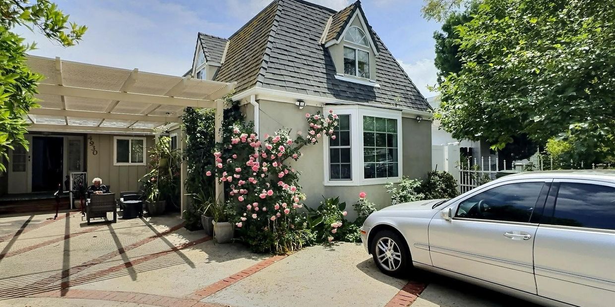 Cozy cottage with a rose bush and a silver car parked outside under a sunny sky.