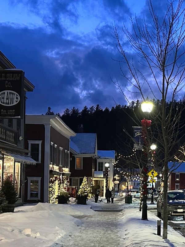 Winter evening on a snowy town street with festive lights and decorated shops.