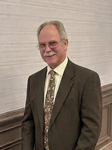 Older man in a suit smiling.