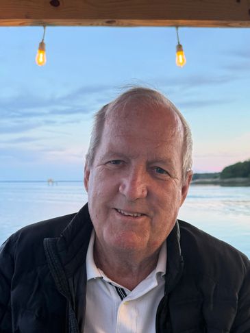 Smiling man with a waterfront backdrop during sunset.
