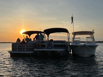 Three boats together on water during a sunset with people relaxing.