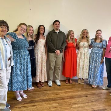 Group of people smiling indoors, dressed in casual and semi-formal attire.