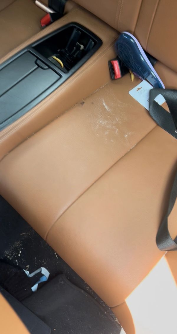 Car back seat with tan leather and some debris including a shoe and a tag.
