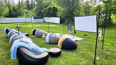 Backyard movie night rental with outdoor screen, lounge seating, blankets, and string lights.