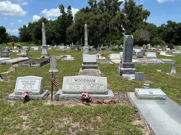 A peaceful cemetery with gravestones and flowers under a blue sky.