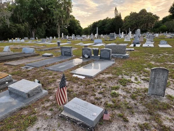 A peaceful cemetery at sunset with American flags on some graves.
