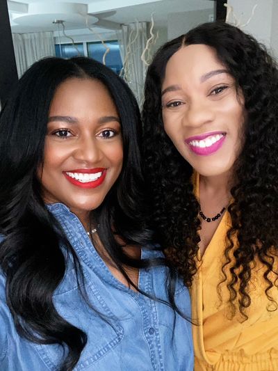 Two smiling women with long hair posing for a selfie indoors.