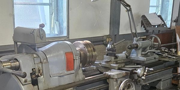 A large metal lathe machine inside a workshop with windows in the background.