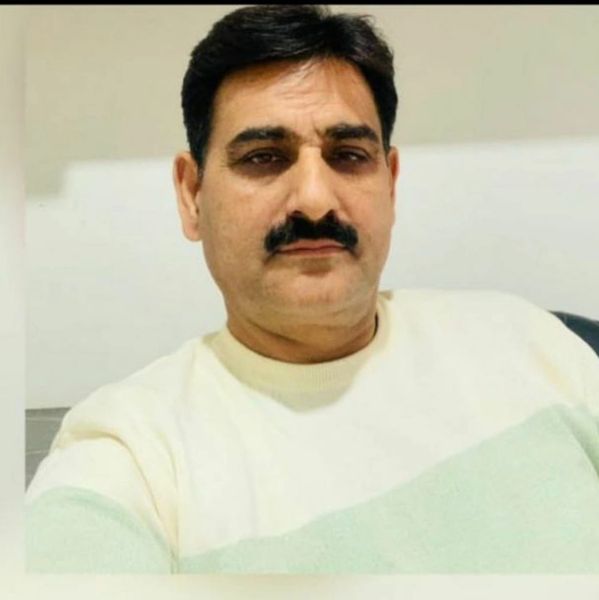 A man with a mustache wearing a light-colored sweater.