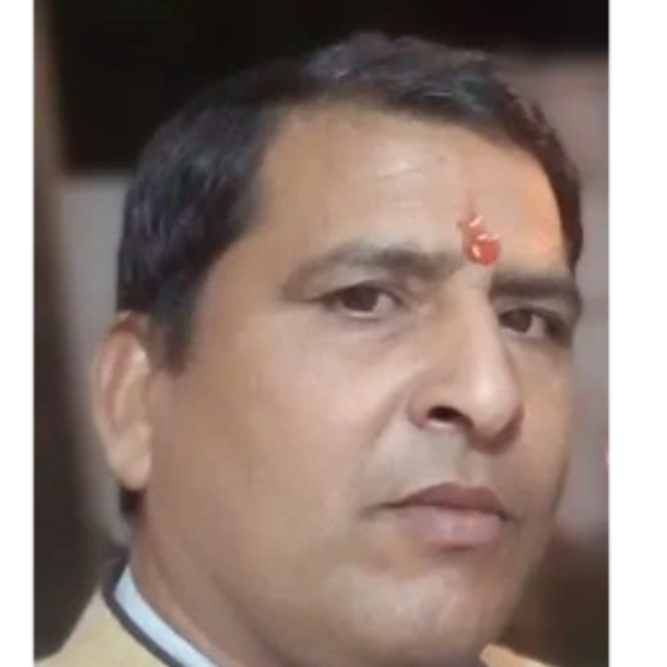 Middle-aged man with a tilak on forehead wearing a beige jacket.