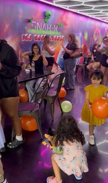 Kids and adults enjoy a colorful party room with balloons and neon decorations.