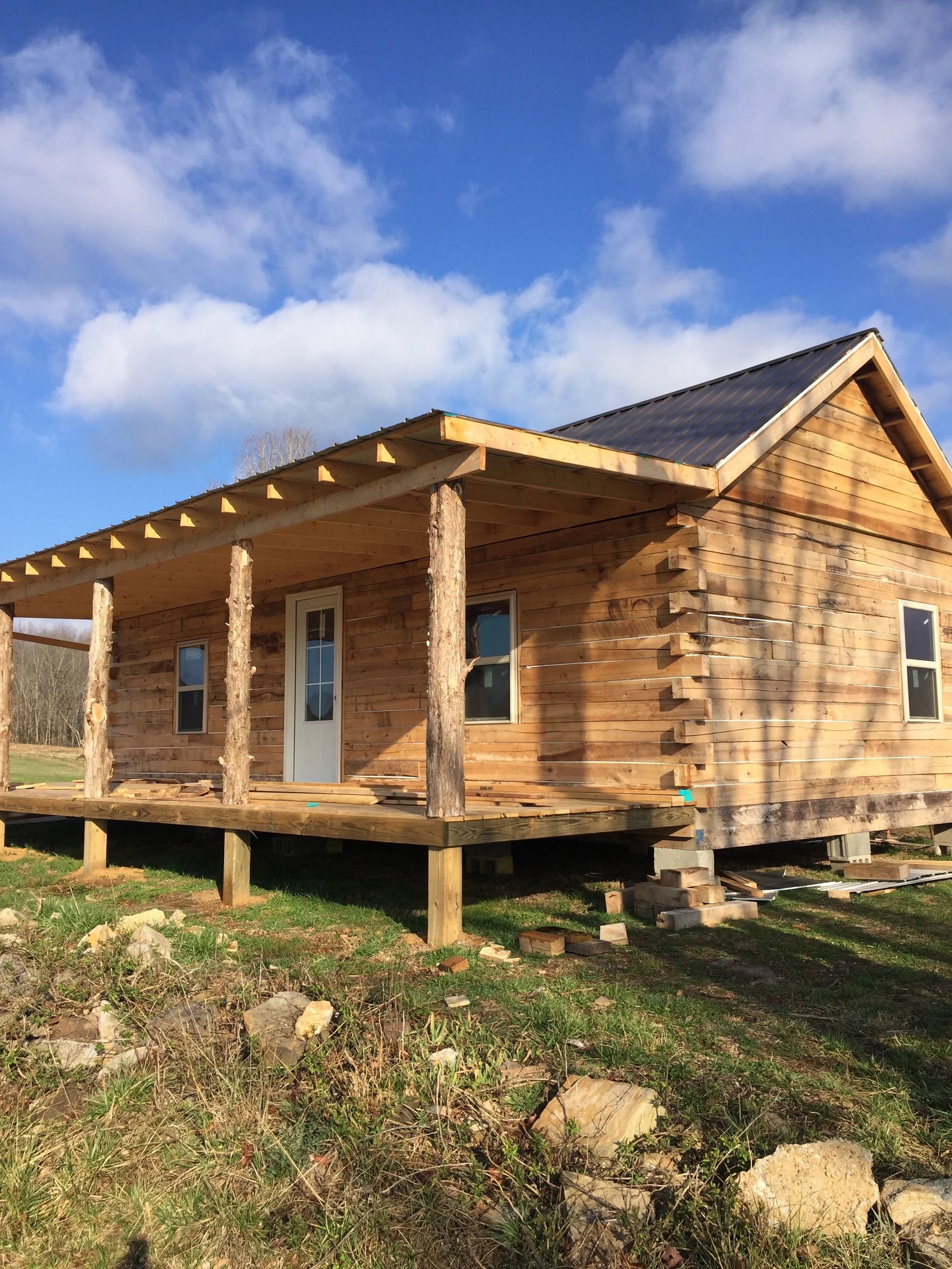 A small wooden cabin with a porch and a grassy area in front of it.