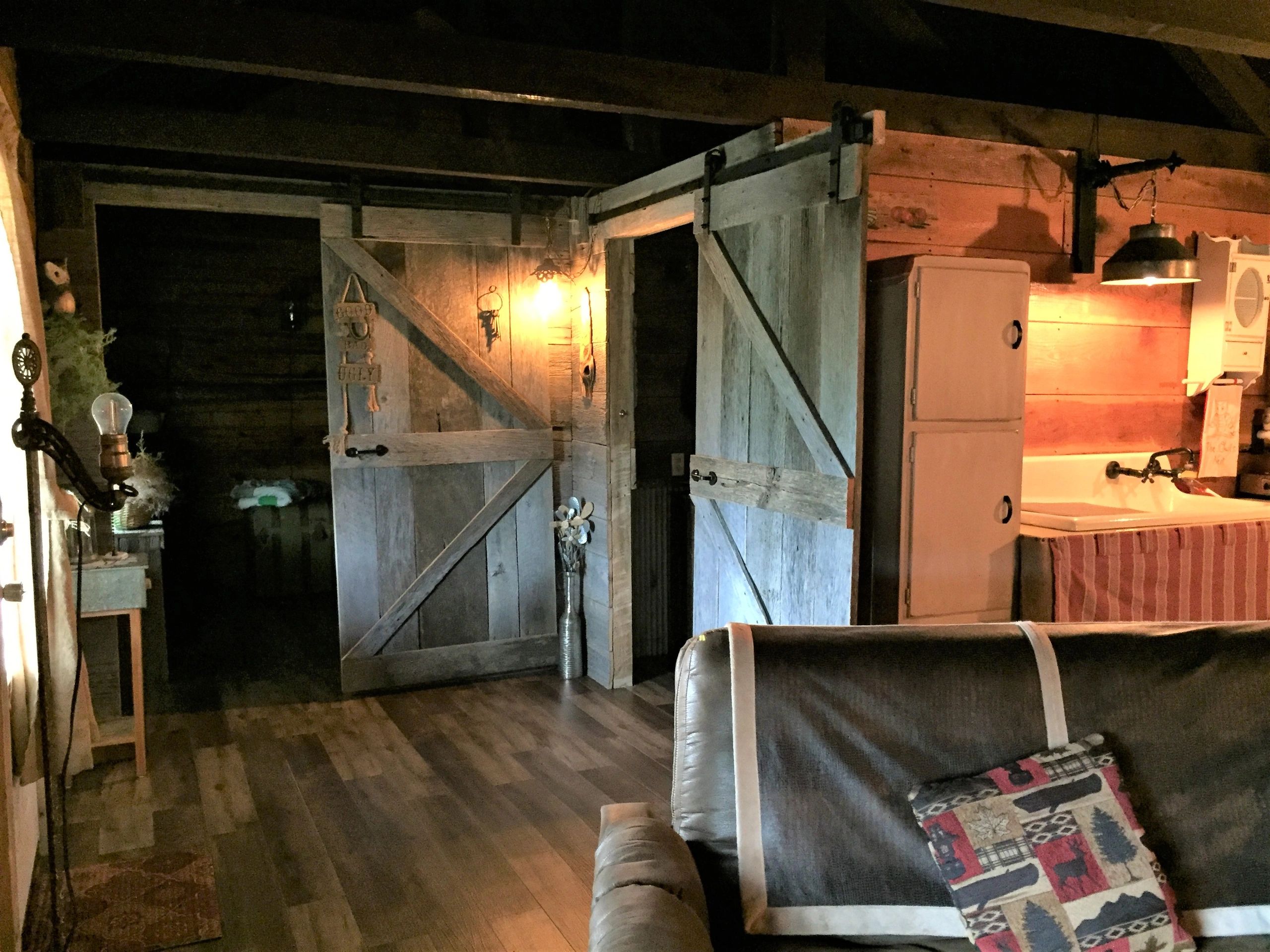 A rustic interior with wooden beams, barn doors, a couch, and a kitchenette.