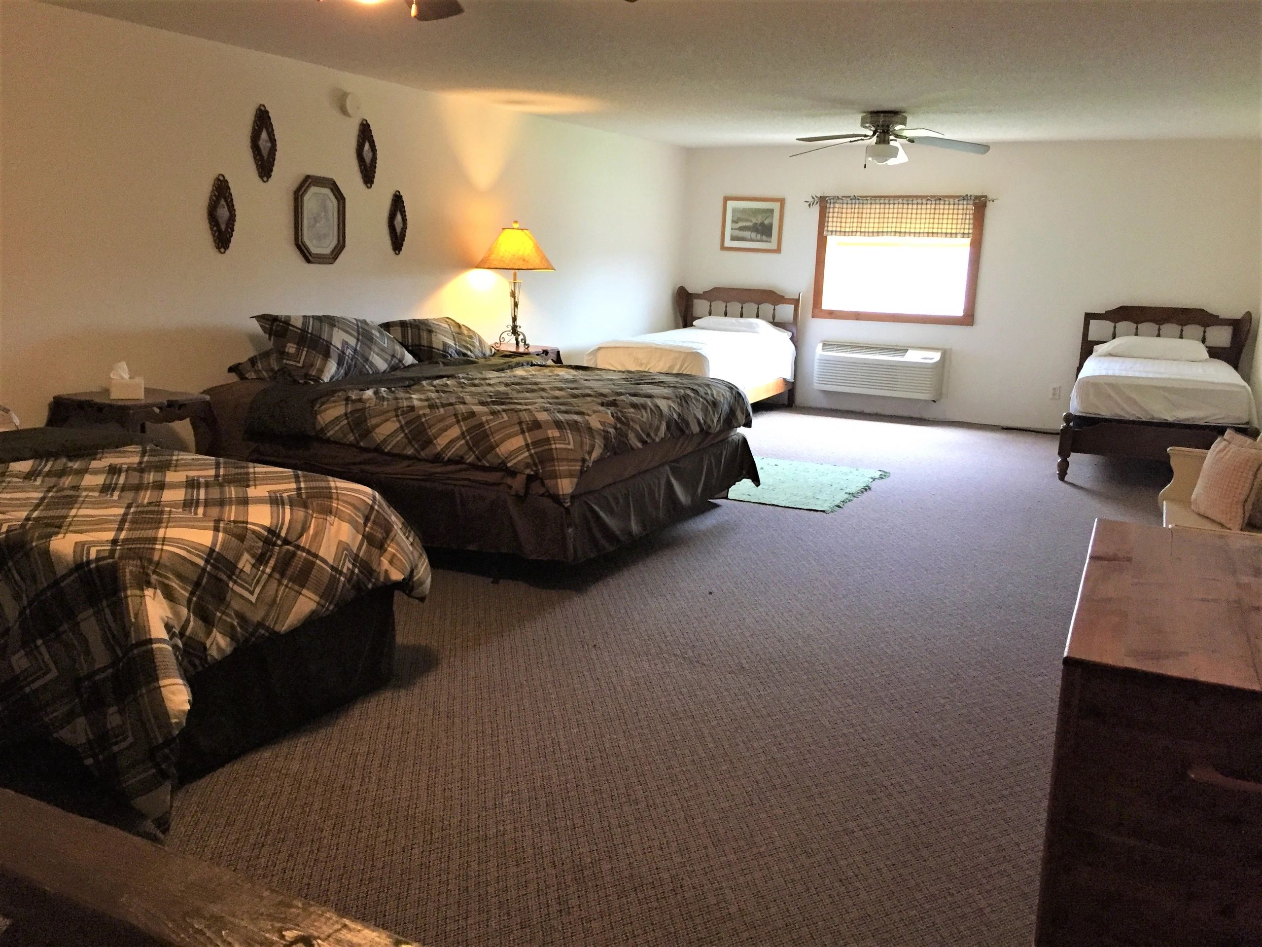 A wide view of a hotel room with three beds, two nightstands, and a dresser.