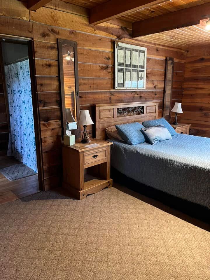 A wide-angle view of a cozy log cabin room with a large bed, nightstands, and a bathroom doorway.