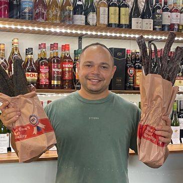 Man smiling, holding two bags of dried meat sticks in a liquor store.