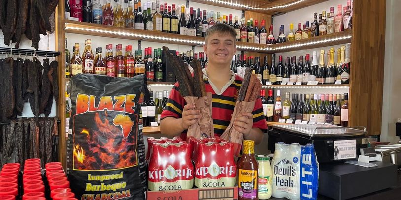 South African man holding bags of biltong and droëwors surrounded by South African products