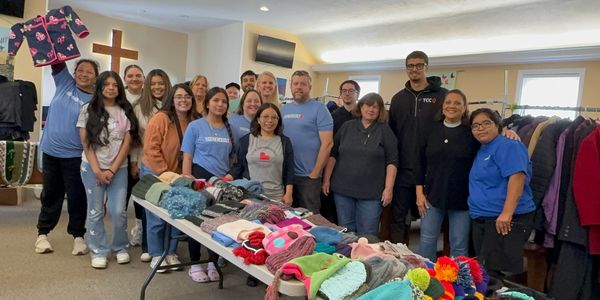 Group of volunteers standing behind a table with donated winter hats and scarves.