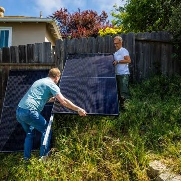 Two men install a solar panel on a sunny hill.