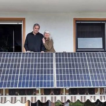 Couple standing behind solar panels on a balcony.