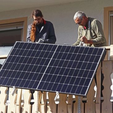 Two men installing a solar panel on a balcony.