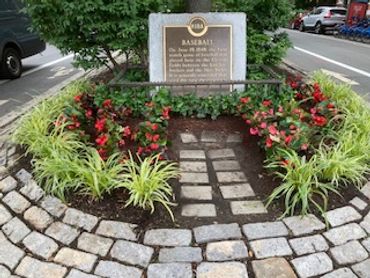 Historic baseball marker surrounded by flowers and stone path.