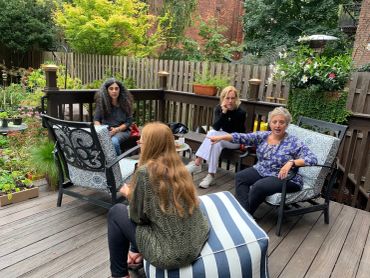 Four women chatting on a wooden deck in a garden.