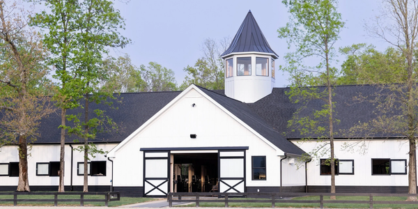 A modern white barn-style building with trees around it under a clear sky.